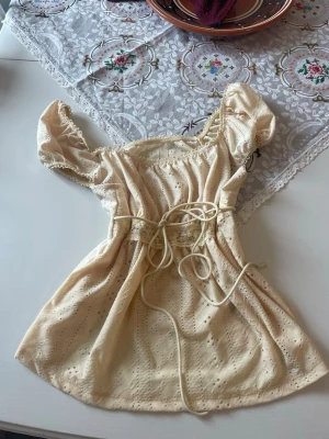 Ljusgul blus med puffärm och snörning - Supersöt ljusgul blus med puffärmar och broderade detaljer. Toppen har snörning i midjan för en feminin siluett och är tillverkad i ett lätt bomullstyg med spetskant. Perfekt för dig som gillar romantisk och vintage-inspirerad stil.