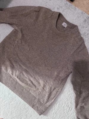Beige stickad tröja från H&M - Mysig beige stickad tröja från H&M i regular fit. Tröjan har rund halsringning, långa ärmar och ribbade muddar vid ärmslut och nederkant. Perfekt för lager på lager och enkel att matcha med olika outfits.