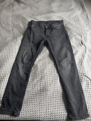 Grå jeans från Nudie Jeans - Snygga grå jeans från Nudie Jeans med klassisk femficksdesign och dragkedjegylf. Jeansen har en tvättad look och raka ben, perfekta för en avslappnad och trendig stil.