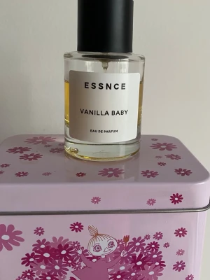 ESSNCE Vanilla Baby Eau de Parfum - ESSNCE Vanilla Baby Eau de Parfum i en rund glasflaska med svart lock. Parfymen har en ljusgul vätska och enkel, stilren etikett med svart text. Doften har tydliga vaniljtoner och flaskan rymmer en generös mängd parfym. Mängd enl bild. Har förvarats mörkt och svalt 