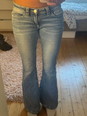 Lågmidjade bootcut jeans  - Säljer ett par lågmidjade ljusblåa bootcut jeans. Jeansen har en snygg tvättad look och utsvängda ben. Från Gina tricot från deras 14+ serie och är i Stolek S. Perfekta till sneakers eller boots för en avslappnad stil.