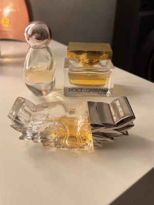 Parfymflaskor i unik design - Tre snygga parfymflaskor i glas, varav en med guldlock och Dolce & Gabbana-etikett, en med rund silverkula som lock och en med kristalliknande form och silverdetaljer. Alla har elegant och modern look, perfekta som inredningsdetalj.