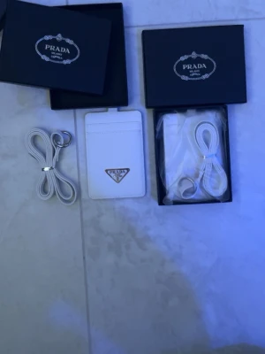 Vit korthållare med band - Snygg vit korthållare  med klassisk trekantig logga i silver framtill. Plånboken har flera kortfack och kommer med matchande vit rem. Perfekt accessoar för att hålla koll på dina kort med stil.