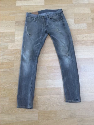 Dondup Jeans - Snygga grå slim jeans med  slitningar som gjorts i fabrik och distressed detaljer på både fram- och baksida. Jeansen har fem fickor och en klassisk knappgylf. Perfekta för en avslappnad och trendig look. Nypris 3499kr