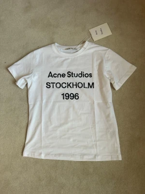 Vit Acne Studios t-shirt Stockholm - Vit t-shirt från Acne Studios med svart text 'Acne Studios STOCKHOLM 1996' på framsidan. 
