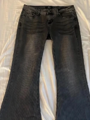 Grå bootcut jeans  - Säljer ett par grå bootcut jeans från R by EMP med klassisk femficksmodell och snygg slitning framtill. Jeansen har breda ben och är tillverkade i denim med en cool tvättad look. Perfekta för dig som gillar retrostil och vill sticka ut. Super snygga!