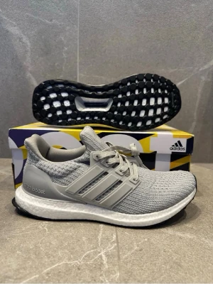 Grå Adidas Ultra Boost sneakers - Snygga grå Adidas Ultra Boost sneakers med stickad ovandel i mesh, vita Boost-mellansulor och svarta yttersulor. Klassiska tre ränder på sidan och snörning. Perfekta för dig som gillar stilrena och bekväma sneakers.
