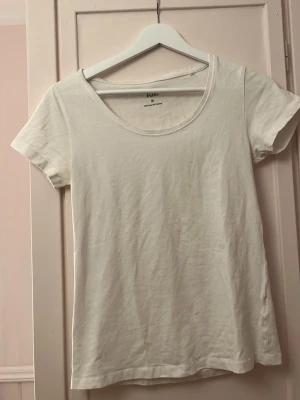Vit basic t-shirt med rund hals - En enkel vit t-shirt med rund halsringning och korta ärmar. Tillverkad i mjuk bomull som känns skön mot huden. Perfekt att matcha med jeans eller shorts för en clean och avslappnad stil.