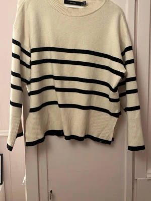 Randig stickad tröja från Vero Moda - Säljer en krämvit stickad tröja från Vero Moda med svarta horisontella ränder. Tröjan kan ha små små fläckar men som man inte tänker på, se exempel på bild 3 