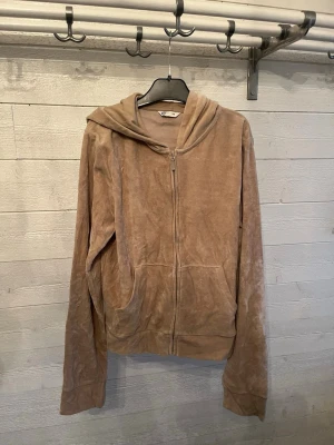 Beige velourhoodie med dragkedja - Mysig beige hoodie i mjuk velour med dragkedja framtill och två fickor. Modellen har huva och långa ärmar, perfekt för en chill och avslappnad stil. Passar dig som gillar neutrala färger och sköna material.