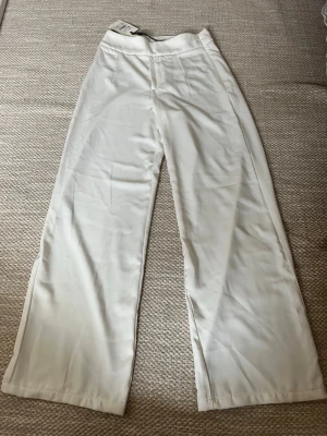 Vida vita linnebyxor - Säljer ett par snygga linnebyxor i vitt med hög midja och raka, vida ben. Byxorna har en enkel och clean look utan synliga fickor eller detaljer, perfekta för en avslappnad och trendig stil. Materialet är lätt och luftigt linne.