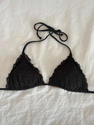 Svart triangeltopp med knyt - Säljer en svart trekantsbikinitopp med snygga spetsdetaljer och knyt både i nacken och ryggen. Bikinin har ett feminint mönster och tunna band som ger en klassisk och stilren look. Perfekt för sommaren och strandhäng! Stor ej storlek men skulle säga S🫶🏼