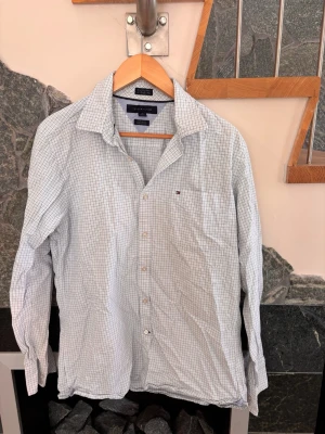Rutig skjorta från Tommy Hilfiger - Klassisk långärmad skjorta från Tommy Hilfiger i vitt med tunna blå och gröna rutor. Skjortan har knappar framtill, bröstficka med liten logga och en bekväm custom fit. Perfekt för en clean och stilren look.