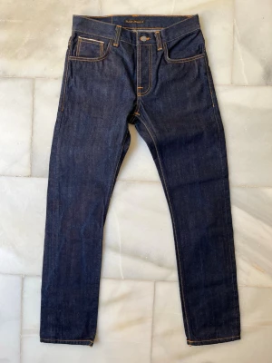 HELT NYA DRY SELVAGE jeans ifrån Nudie Jeans  - Säljer ett par HELT NYA Dry Selvage jeans ifrån Nudie Jeans. Jeansen är aldrig använda. En lapp är felsydd (blev fel i deras produktion se bild 7). ✌🏼—————————————————————                                                                      📐| Storlek: 30-30                                                   👖| Märke: Nudie jeans                                         🔎| Skick: HELT NYA!                                                  💵| Ny Pris: 2500kr                    