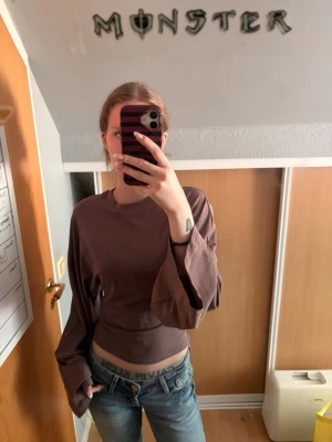Brun långärmad croppad topp - Säljer en enkel och stilren brun långärmad topp med croppad passform. Toppen har rund halsringning och är tillverkad i ett mjukt, stretchigt material som känns skönt mot huden. Perfekt att matcha med jeans eller kjol för en avslappnad look.