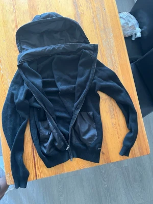 Svart cardigan med dragkedja och fickor - Säljer en svart cardigan med luva eftersom jag vuxit ur den, jättefin bra nu till hösten och våren till för dig som vill ha det där extra till stilen. Inga tydliga tecken på användning eller så. Kom privat för pris.