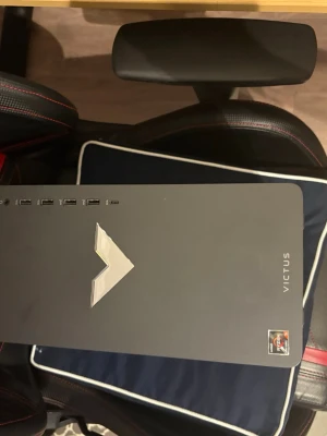 HP Victus 15L stationär dator - Säljer en HP Victus 15L stationär dator i svart med stilren design och en rgb V-logga på framsidan. Datorn har flera USB-portar på framsidan och AMD Ryzen-märke. Perfekt för gaming eller studier tack vare bra prestanda och kompakt format.