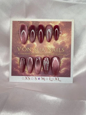 Satin (M);Medium Almond - Snygga handgjorda press-on naglar i vinröd jelly+cateye med vita rosetter. Medel Långa, mandelformade naglar som ger en unik look. Perfekta för dig som vill sticka ut med stilrena detaljer och trendig design.M: 16 mm, 12 mm, 12,5 mm, 11,5 mm, 10 mm