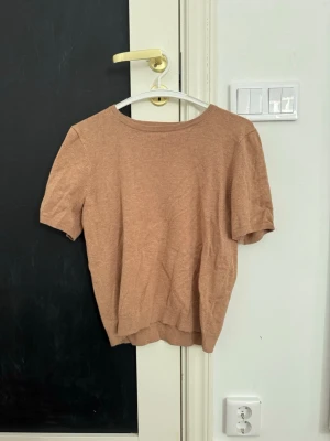 Beige stickad topp med kort ärm - En enkel och stilren beige stickad topp med korta ärmar och rund halsringning. Perfekt att matcha med jeans eller kjol för en avslappnad look. Materialet är mjukt och lätt, vilket gör den skön att bära under varmare dagar.