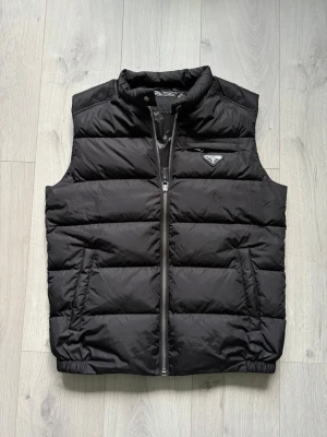 Re-Nylon Padded Vest - Svart dunväst från Prada. Använd sparsamt i extremt fint skick och helt fri från fläckar, hål osv. Storlek 48 vilket motsvarar en M. 