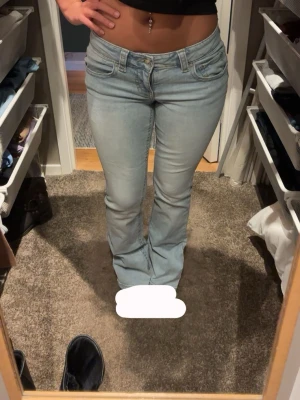 Ljusblå bootcut jeans - Säljer ett par ljusblå bootcut jeans med låg midja och klassiska fem fickor. Jeansen har en snygg tvätt och fickor med lock och knapp bak. Perfekta för dig som gillar en retro och avslappnad stil.