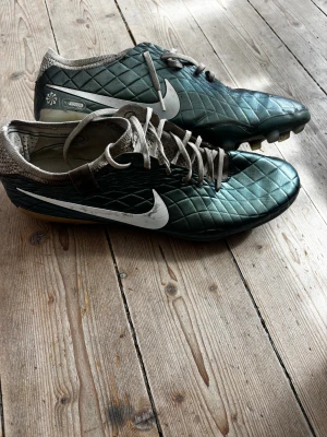 Nike Tiempo limited edition ormskinn  - Snygga fotbollsskor från Nike i metallicgrönt med vita detaljer och klassisk Nike-logga på sidan. Skorna har snörning, quiltad ovandel och dobbar för bra grepp på planen. Perfekta för dig som vill sticka ut på fotbollsplanen.