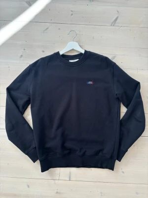 Ami Paris tröja  - En stilren svart sweatshirt från Ami med broderad logga i blått, vitt och rött på bröstet. Bra skick med en liten defekt i fram, inget som syns när man bär tröjan. Se sista bilden. 