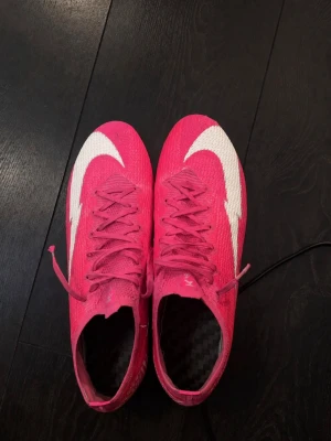 Rosa mbappe elite fotbollsskor med vita detaljer - (Pris kan diskuteras)Snygga fotbollsskor i starkt rosa med stora vita swoosh-detaljer på ovansidan och silvriga dobbar undertill. Skorna har snörning och en strömlinjeformad design för bästa passform på planen. Ovandelen är i ett lätt syntetmaterial som ger bra bollkontroll.