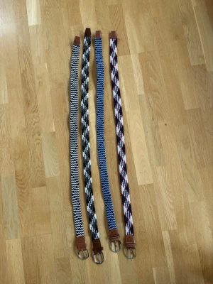 Fyra mönstrade flätade bälten 120KR STYCK - Säljer fyra snygga flätade bälten i olika färger och mönster. Bältena har metallspännen och detaljer i brunt skinn. Perfekta för att ge din outfit en cool touch med randiga och rutiga mönster i svart, vitt, blått och rött.
