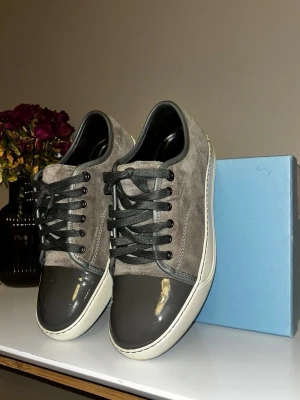 Grå sneakers med mocka och lack - Super snygga gråa lanvins i storlek 6/41 eu, mockan, sulorna och toe capen är i super bra skicka inga anmärkningar enligt mig, tveka inte på att höra av er vid funderingar! Dustbag och box ingår 