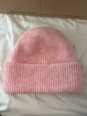 Rosa ribbstickad mössa - Mysig rosa mössa i ribbstickat material med bred uppvikt kant. Klassisk form som sitter skönt på huvudet och ger en avslappnad vibe. Perfekt för kalla dagar när du vill hålla dig varm och ändå se snygg ut. Passar till de flesta outfits och är superenkel att matcha.
