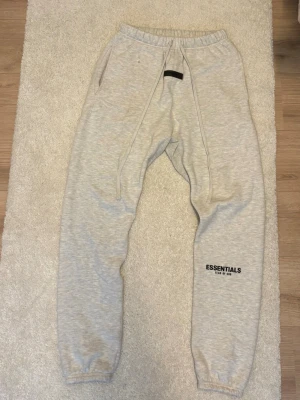 ❄️Gråa Essentials mjukisbyxor❄️ - Säljer ett par ljusgrå mjukisbyxor från Fear of God Essentials. Byxorna har resår i midjan, dragsko, muddar vid bensluten och två sidofickor. Essentials-loggan är tryckt på vänster ben. Perfekta för chill dagar och streetwear-stil. Xs kan vara är mer baggy, Du Siam har S passar perfekt.