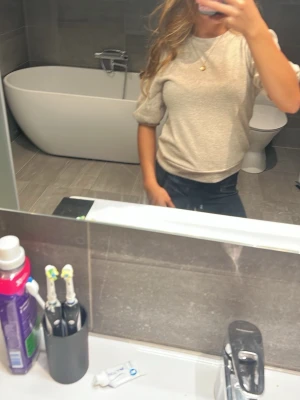 Beige puffärm topp - Säljer en beige topp med puffärmar och rund hals. Toppen har en loose passform och är tillverkad i ett mjukt material som känns skönt mot huden. Perfekt att styla med jeans eller kjol för en trendig look.