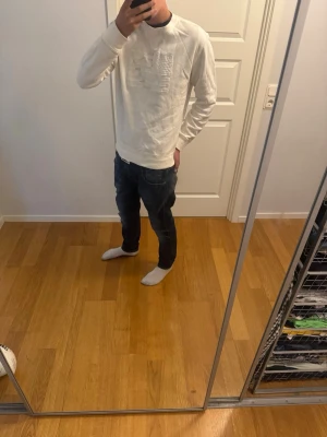 Vit sweatshirt med broderad flagga - Vit sweatshirt från Polo Ralph Lauren med rund halsringning och broderad amerikansk flagga på bröstet. Tröjan har långa ärmar och ribbade muddar vid ärmslut och nederkant. Perfekt för en avslappnad och stilren look.