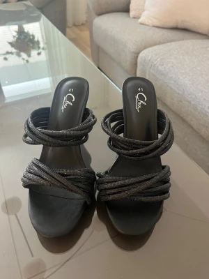 Svarta pumps med flätade remmar - Snygga svarta pumps från Dinsko med höga klackar och flera flätade remmar över foten. Öppen tå och slip-in modell som ger en trendig look. Tillverkade i konstläder med textilremmar för en cool och modern känsla.