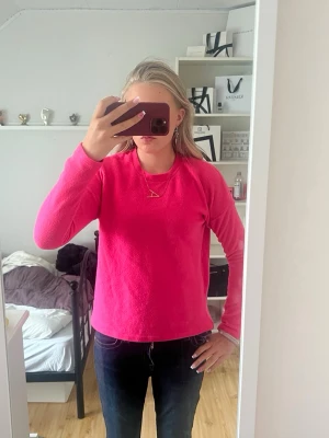Knallrosa fliströja  - En fliströja  i starkt rosa färg med rund hals och långa ärmar. Materialet är mjukt och fluffigt, vilket gör den riktigt skön att ha på sig. Enkel design utan synliga detaljer eller mönster, perfekt för dig som gillar färgstarka plagg.