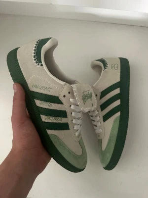  Stüssy x Adidaswales Bonner - Unika sneakers i samarbete mellan Stüssy och Adidas. Beige mocka med gröna detaljer, gröna ränder och sula. Stüssy-logga på plössen. Kontakta vid info storlek 41 1/2. Känns som 42. Kontakta vid mer info. Kvitto går att lösa