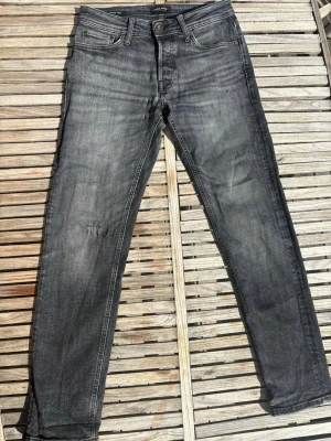Grå slim fit jeans från Jack and Jones i 30 32 - Snygga grå slim fit jeans med klassisk femficksdesign och diskret slitning på låren. Jeansen har normal midja och raka ben, perfekta till en avslappnad stil. Tillverkade i mjuk denim med lite stretch för extra komfort. 