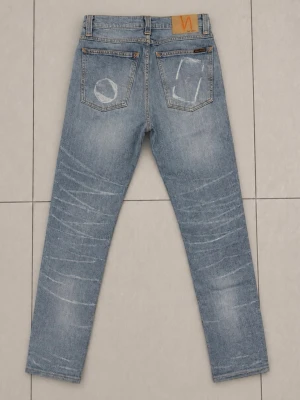 Nudie Jeans 30/34 - Ljusblå jeans med raka ben och tydliga slitningar på både fram- och baksida. Jeansen har klassisk femficksdesign och kontrastsömmar. Materialet är denim och de har en avslappnad vibe med unika detaljer på bakfickorna.