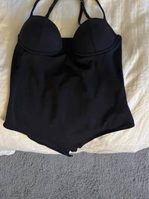 Svart body med vadderade kupor - Snygg svart body med tunna axelband och vadderade kupor för extra stöd. Bodyn har en enkel, stilren design och är tillverkad i ett stretchigt material som sitter skönt mot kroppen. Perfekt att styla under en skjorta eller kavaj. Helt oanvänd 💕