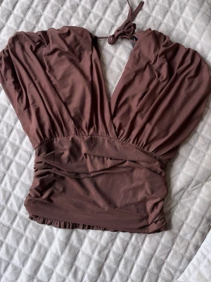 Brun omlottopp med Knut bak - Säljer en brun omlottopp med djup v-ringning och knyt i nacken. Toppen har en åtsittande midja och är tillverkad i ett mjukt, stretchigt material. Perfekt för dig som gillar en trendig och stilren look. Från SHEIN. 