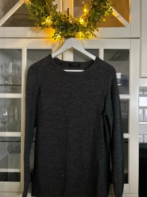 Mörkgrå stickad tröja från Selected - Mörkgrå stickad tröja från Selected med rund halsringning och långa ärmar. Tröjan har en enkel och stilren design, perfekt för lager-på-lager och passar till många olika outfits. Materialet är mjukt och bekvämt.