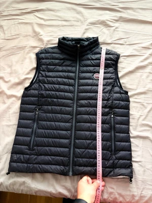 Svart dunväst från Colmar - Snygg svart dunväst från Colmar med quiltad design och hög krage. Västen har två dragkedjeförsedda fickor framtill och Colmar-logga på bröstet. Perfekt för lager-på-lager och håller dig varm utan att bli för tung.