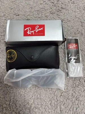 Svarta Ray-Ban solglasögon - Säljer ett par klassiska svarta Ray-Ban solglasögon med mattsvarta bågar. Kommer med originalfodral, putsduk och box. Perfekta för dig som vill ha en tidlös och stilren look i sommar.