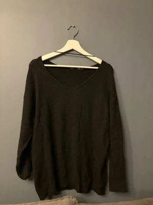 Svart stickad tröja från 157 - Svart stickad tröja från 157 med v-ringning och långa ärmar. Tröjan har en avslappnad passform och är lite off shoulder på ena sidan. 