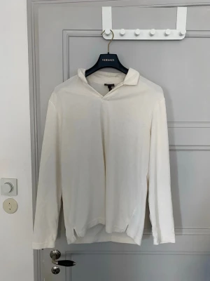Vit långärmad skjorta med krage - Stilren vit långärmad skjorta med mjuk krage och relaxed fit. Skjortan har en enkel design utan synliga knappar och är tillverkad i ett mjukt material som känns skönt mot huden. Perfekt för en clean och avslappnad look.