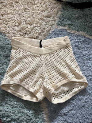 Vita strand shorts med resårmidja - Säljer ett par vita strand shorts med bred resår i midjan och mjukt innerfoder. Shortsen har ett sportigt och luftigt utseende, perfekta för stranden. Stilen är loose och materialet känns syntetiskt och stretchigt. 