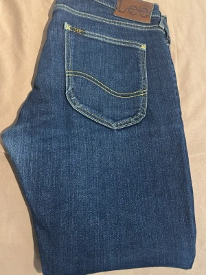 Mörkblå jeans från Lee - Snygga mörkblå jeans från Lee med klassisk femficksdesign och kontrastsömmar. Jeansen har rak passform och är tillverkade i ett mjukt denimtyg som sitter skönt hela dagen. Perfekta till en avslappnad stil.