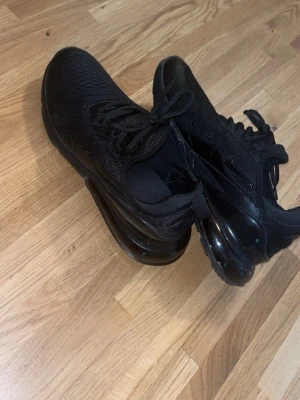 Helvita Nike Air Max 270 sneakers - Säljer ett par helsvarta Nike Air Max 270 sneakers med mesh- och syntetmaterial. Skorna har en chunky sula med synlig Air-enhet och klassisk Nike-logga på sidan. Perfekta för dig som gillar sportig och clean stil. Oanvända/helt nya passar inte mig