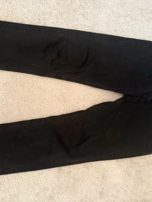 Svarta jeans från Jack & Jones - Säljer ett par svarta jeans från Jack & Jones med klassisk rak passform. Jeansen har normal midja och är tillverkade i ett mjukt bomullsmaterial med lite stretch för extra komfort. Perfekta för dig som gillar en stilren och enkel look. (Litet hål i bakfickan)